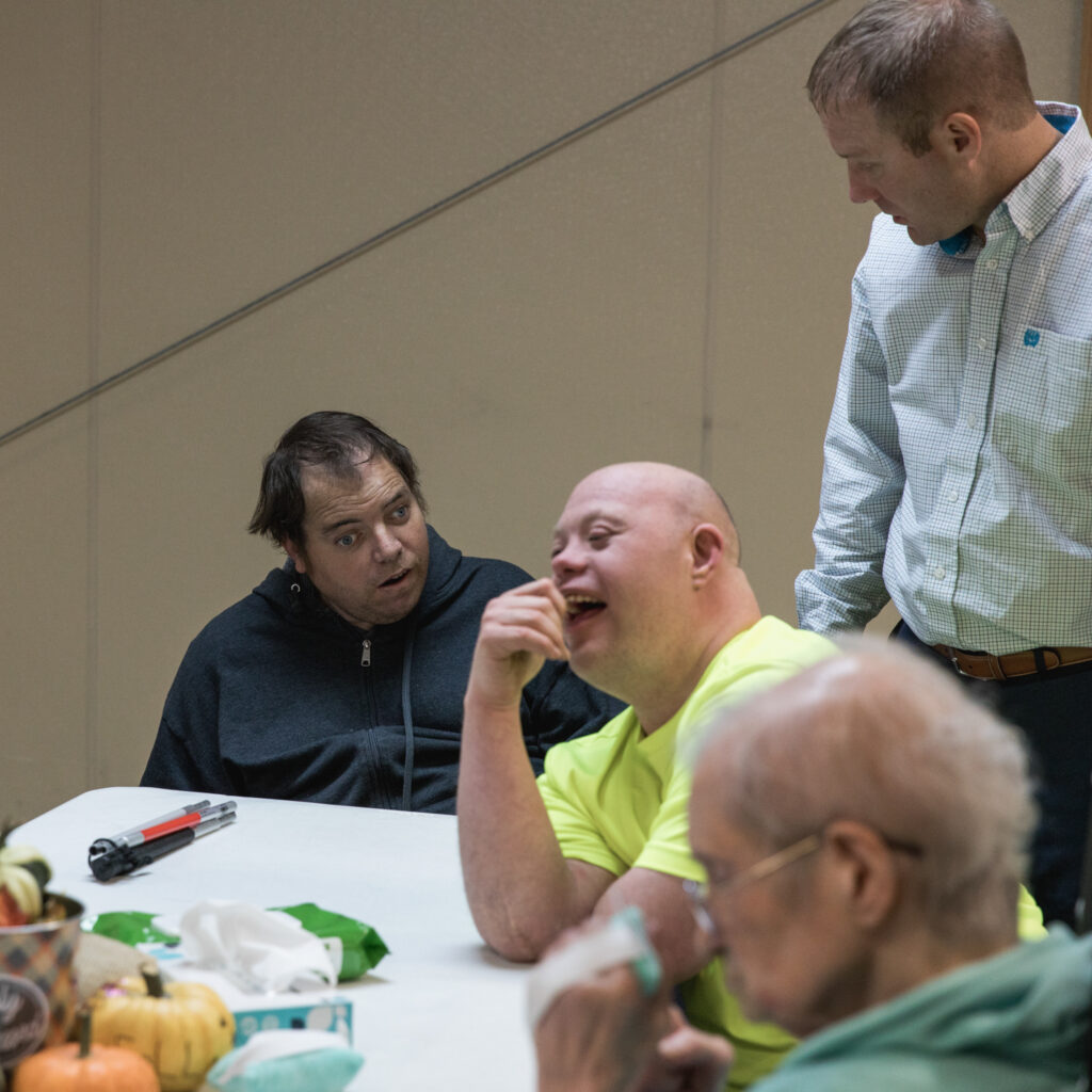 A group of individuals with developmental disabilities sit together at a table in TVDSI's day center in Greenleaf, KS. TVDSI's day center serves adults with intellectual and developmental disabilities.