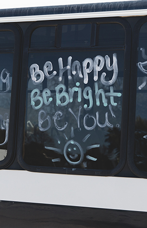 Friendly phrases written on the side of a bus for transportation services for adults with developmental and intellectual disability.